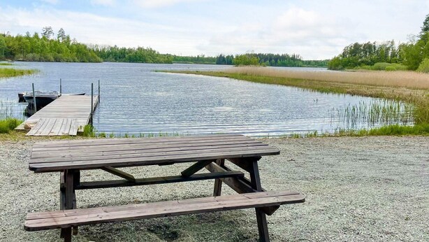 Ein Kiesbereich mit Holztisch und Picknickplatz, eine Anlegestelle ragt in einen stillen See.