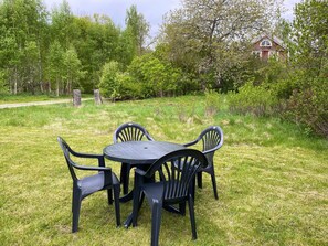 A round table with four chairs in a grassy outdoor area, surrounded by trees and a building in the background. - 5 Person Holiday Home in Emmaboda (Emmaboda)