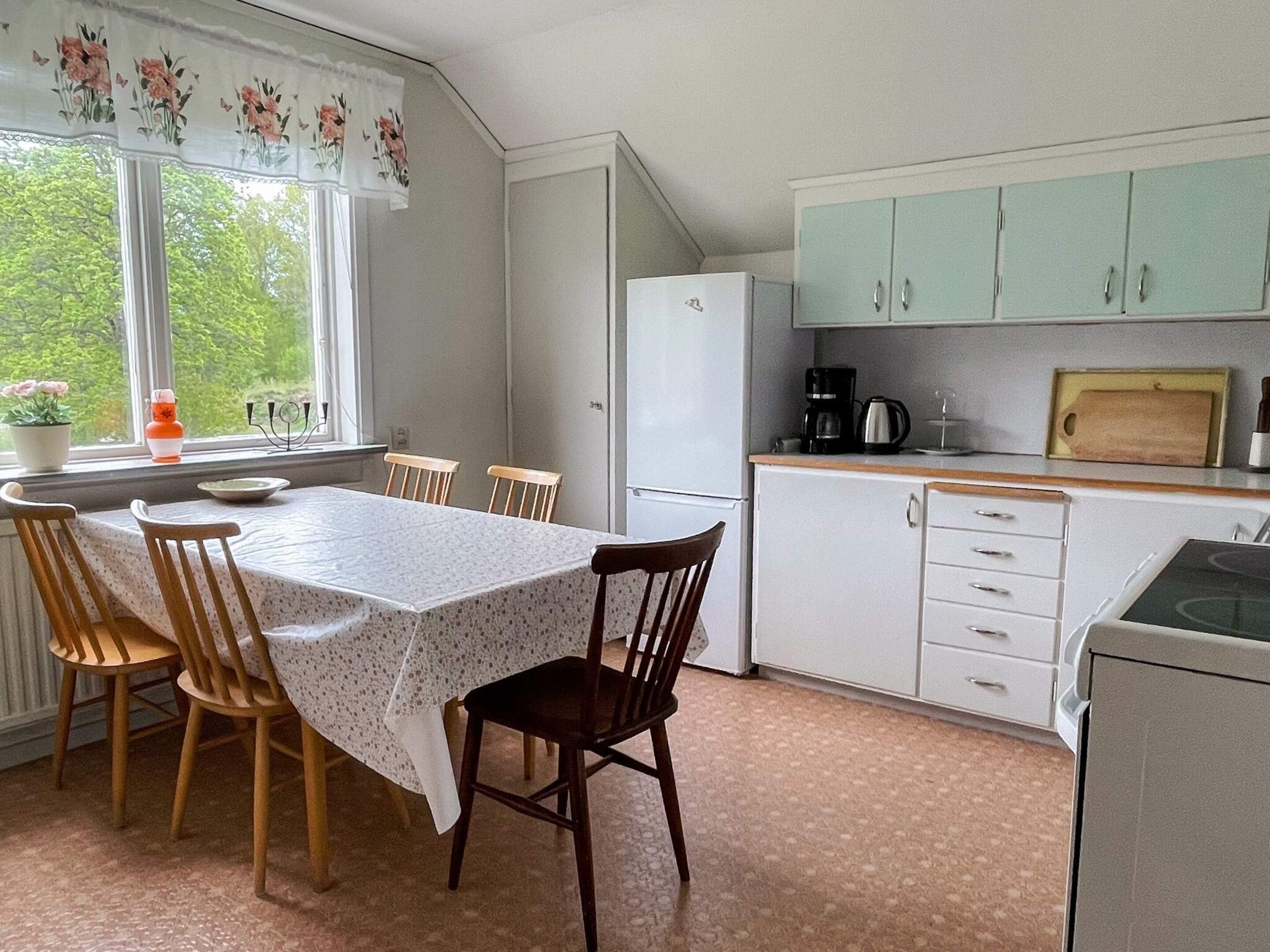 A compact kitchen with a dining table, chairs, a refrigerator, a coffee maker, and cabinets.