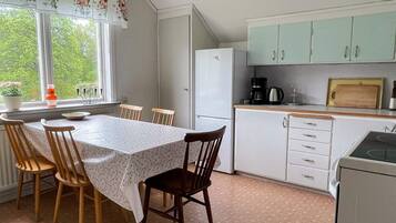 A compact kitchen with a dining table, chairs, a refrigerator, a coffee maker, and cabinets.