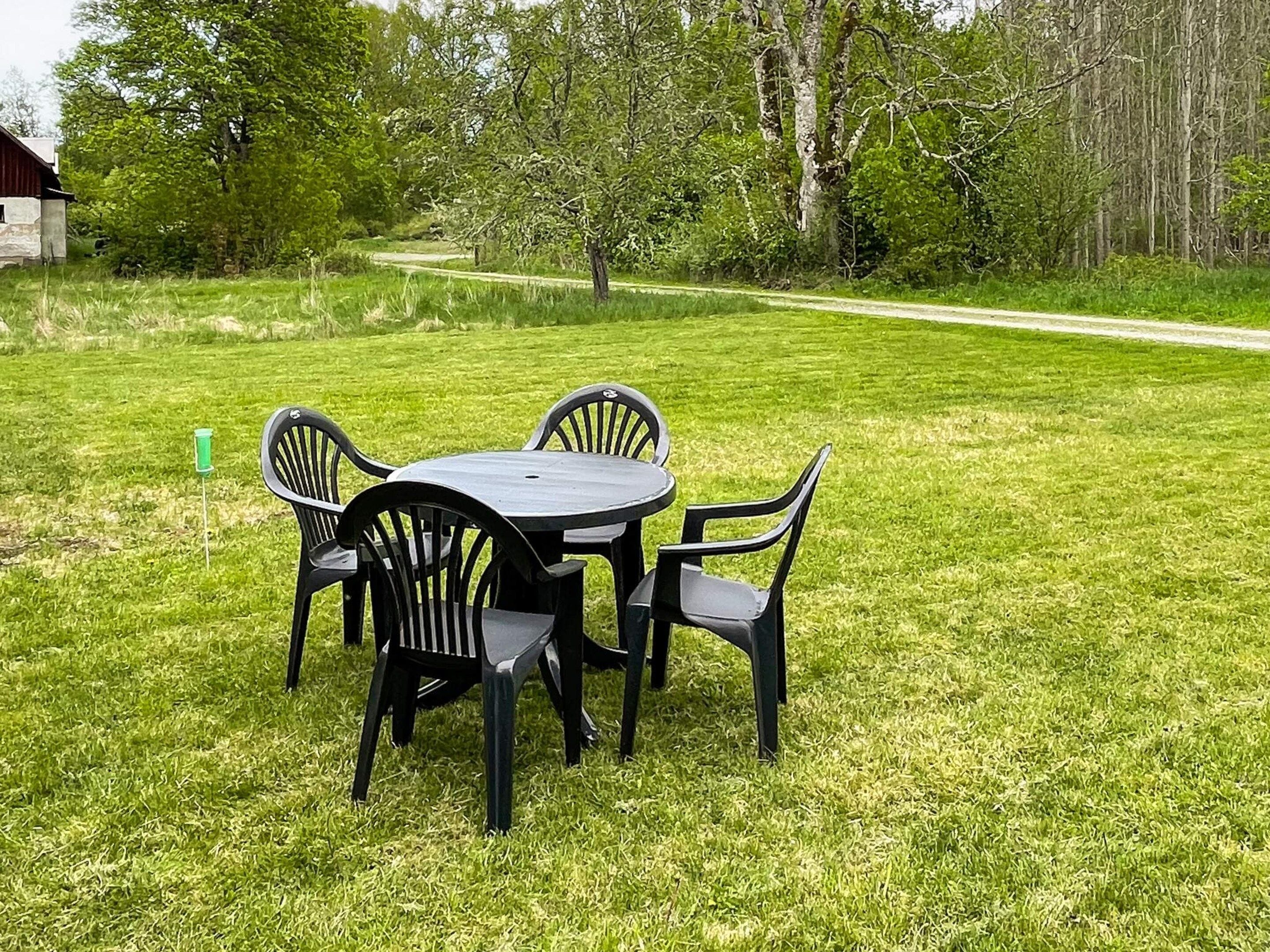 A round table with four chairs in a grassy outdoor area with trees in the background.