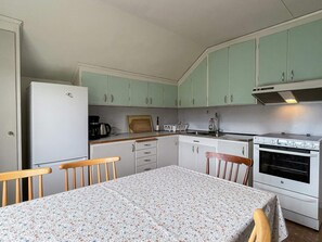 A compact kitchen with a refrigerator, stove, sink, and wooden chairs around a table. - 5 Person Holiday Home in Emmaboda (Emmaboda)