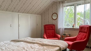 Ein Schlafzimmer mit einem Bett, zwei roten Sesseln, einem Fenster mit Aussicht und einem weißen Kleiderschrank.