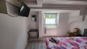 Quarto com uma cama, janela, cadeira, televisão e radiador.
