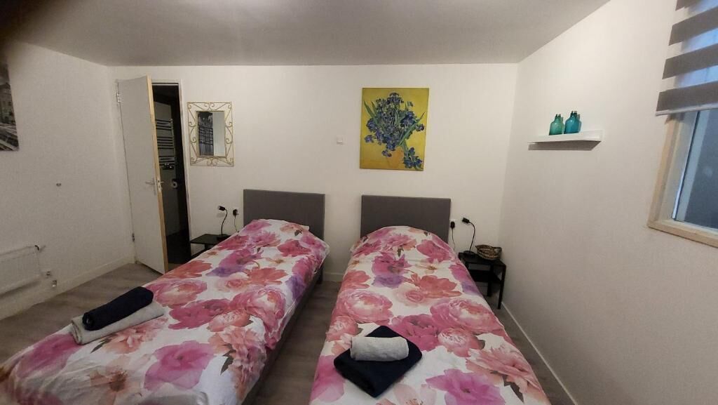 A bedroom with two beds, a mirror, a painting, and a window.