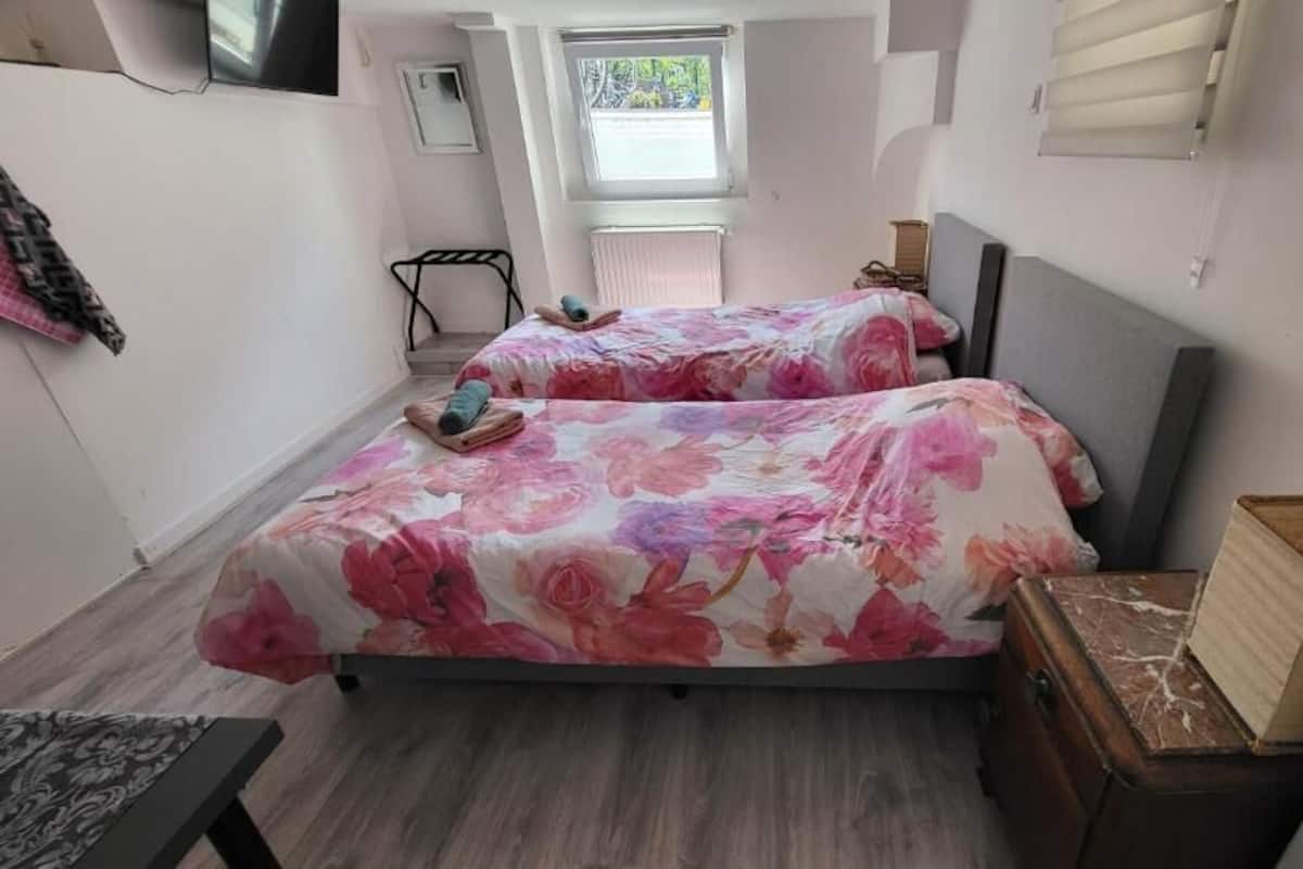 Quarto com duas camas, uma mesinha, uma cadeira, um radiador e uma janela.