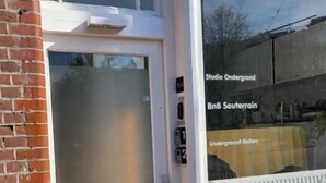En byggnadsingång med en vit dörr, en tegelvägg och ett fönster med en skylt som visar texten ”Studio Underground”.