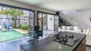 Et moderne køkken med en central ø, et spiseområde med en sofa og en trappe til en overetage.