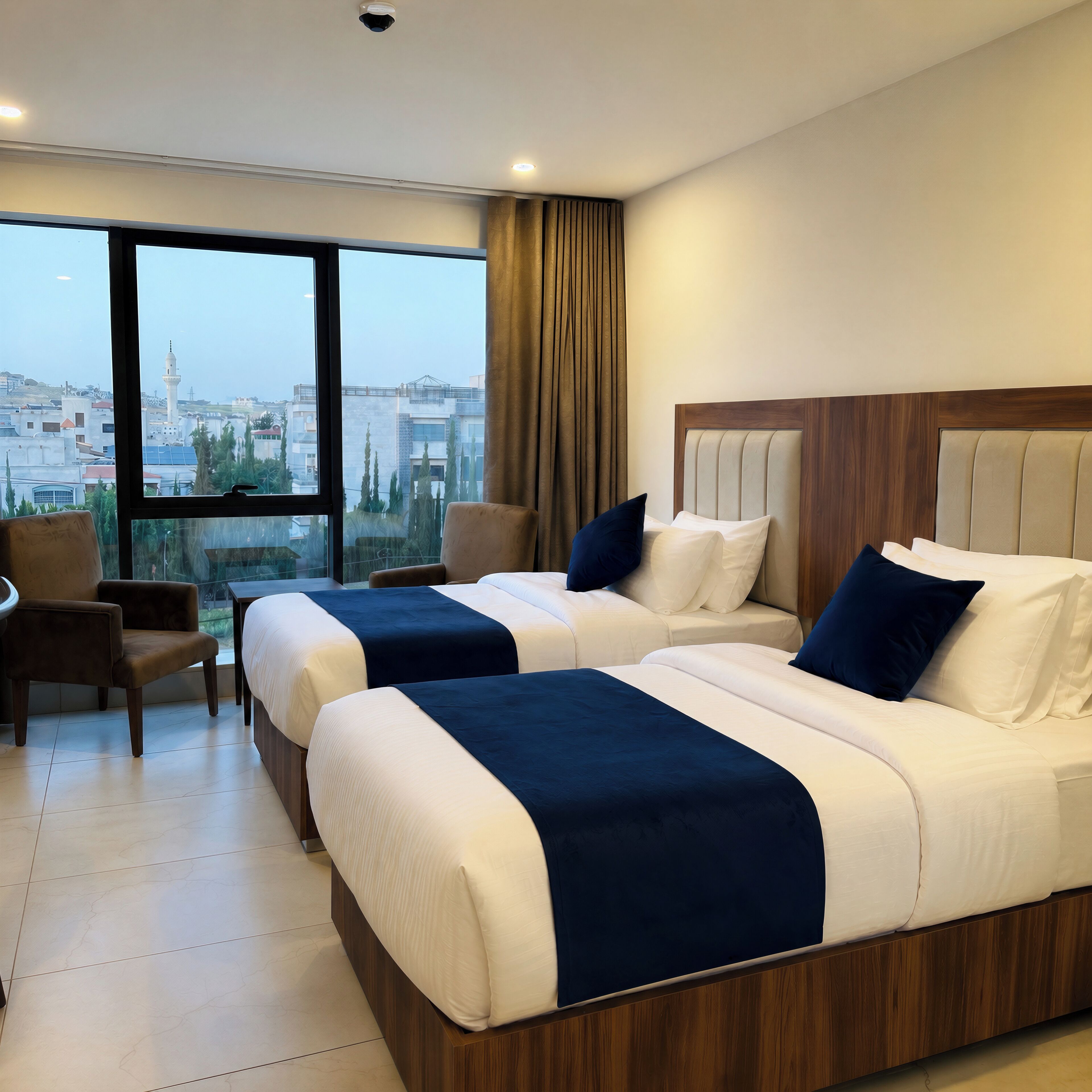 A hotel room with two beds, a chair, a view of the cityscape, and a large window.