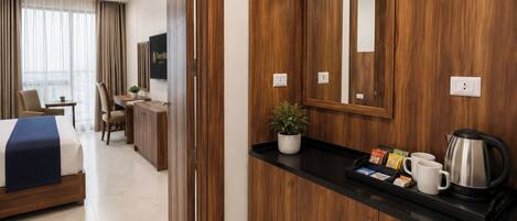 Una habitación de hotel con cama, escritorio, espejo y cafetera.