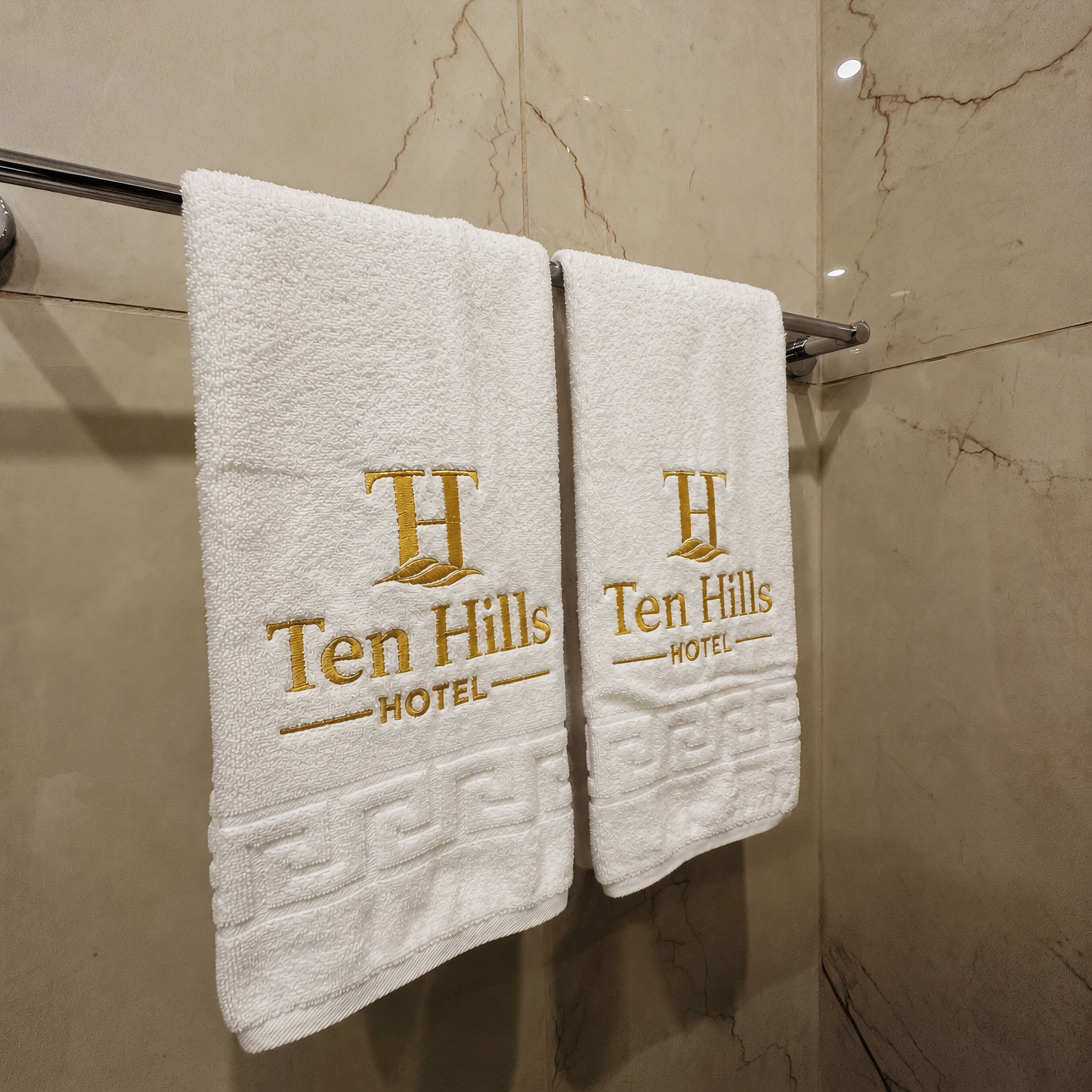 Two white towels hanging on a metal rack with the 'Ten Hills Hotel' logo.