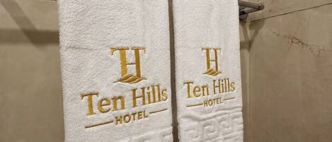 Dos toallas blancas colgadas en un perchero metálico con el logotipo del 'Ten Hills Hotel'.
