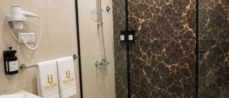 A modern bathroom with a glass-enclosed shower, a white sink, and a towel rack with 'Ten Hills Hotel' towels.