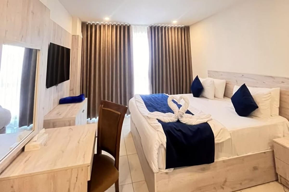 A hotel room with a bed, a desk, a chair, a TV, and curtains.