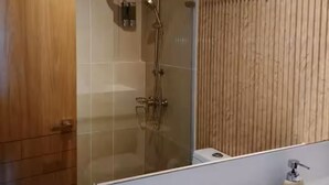 A modern bathroom with a glass-enclosed shower, a wooden panel wall, and a white sink with a soap dispenser. - Baia Kristal Experience Apartment (Cartagena)