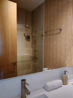 Een moderne badkamer met een douchecabine van glas, een wand van houtpanelen en een witte wasbak met zeepdispenser.