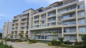 A multi-story residential building with balconies, a paved driveway, and landscaped areas with small trees. - Baia Kristal Experience Apartment (Cartagena)