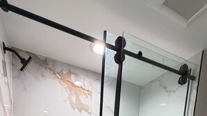 A modern bathroom with a glass shower enclosure, marble walls, and a toilet.