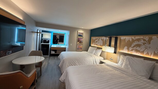 A hotel room with two beds, a TV, a desk, and a bathroom with a mirror.