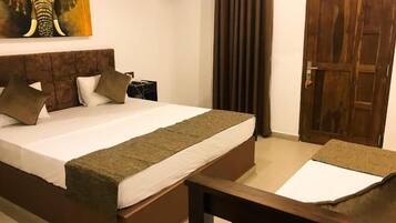 Un dormitorio con cama, almohadas, una colcha, una mesita de noche de madera, un cuadro, una cortina y una puerta de madera.