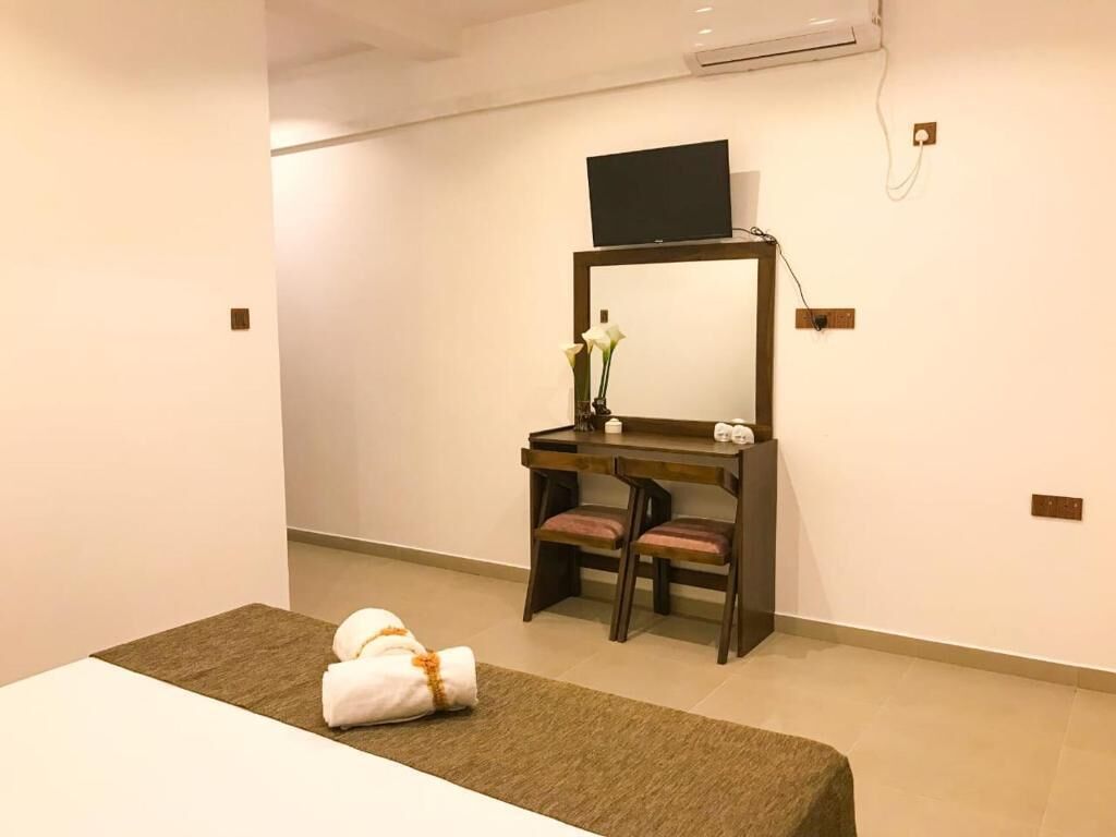 A hotel room with a bed, a desk with a chair, a television, and a vase with flowers.
