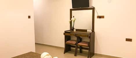 Una habitación de hotel con cama, escritorio, silla, televisor y un florero con flores.