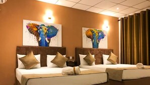 Habitación de hotel con dos camas, cada una con cabecero, ropa de cama blanca y almohadas color beige. Hay dos cuadros colgados en la pared con elefantes.