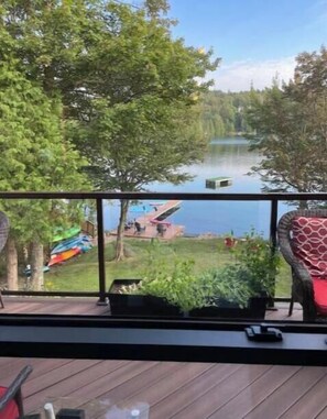 Une terrasse avec vue sur un lac, entourée d’arbres et d’une zone herbeuse agrémentée d’une aire de jeux colorée.