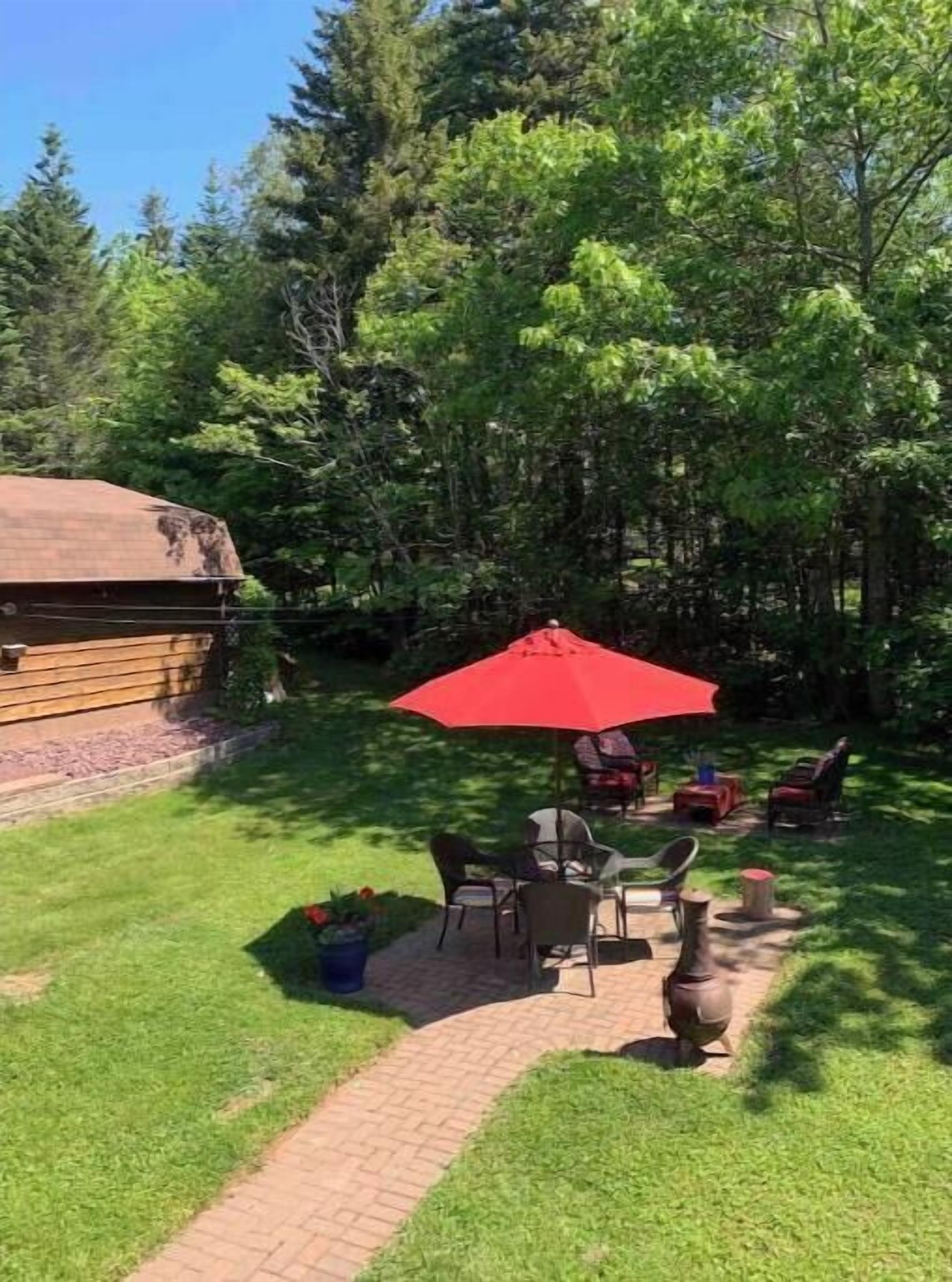 A patio with a red umbrella, outdoor furniture, and a log cabin in a wooded area.