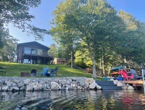 Una propiedad frente al lago con una casa, mobiliario exterior y un muelle.