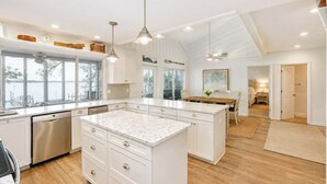 Uma cozinha moderna com uma ilha grande, armários brancos e iluminação pendente.