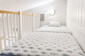 Ein Schlafzimmer mit Etagenbett, weißen Wänden, einem Holgeländer und einer runden Deckenleuchte.