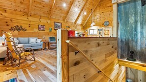 Ein Holzblockhaus-Interieur mit Schlafzimmer auf Schlafgalerie, Essbereich und Wohnzimmer mit Schaukelstuhl.