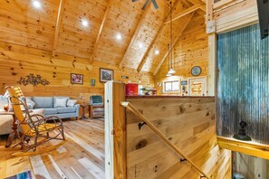 Interior de una cabaña de madera con habitación en el altillo, comedor y sala de estar con mecedora.