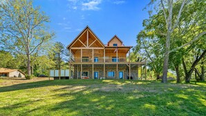 Ein zweigeschossiges Holzhaus mit Balkon, umgeben von Bäumen und einem Rasen.