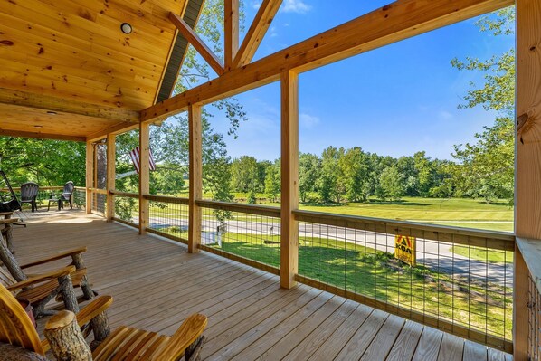 Una terraza techada con vigas de madera, vista a un campo de golf y mobiliario exterior.