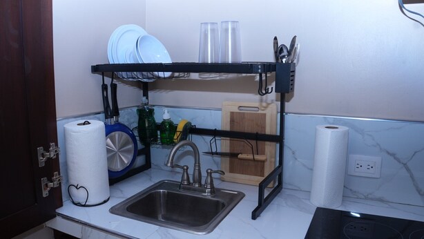 A kitchen with a sink, a dish rack, and a wooden cutting board. - HOTEL LOS AMIGOS  (Puerto Cortés)