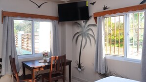 A room with a bed, a dining table with chairs, a TV mounted on the wall, and windows with curtains. - HOTEL LOS AMIGOS  (Puerto Cortés)