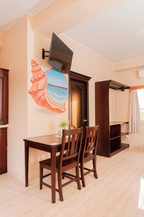 Una habitación con una mesa de comedor, sillas, un televisor de pantalla plana en la pared y una gran obra de arte decorativa con forma de caracola.