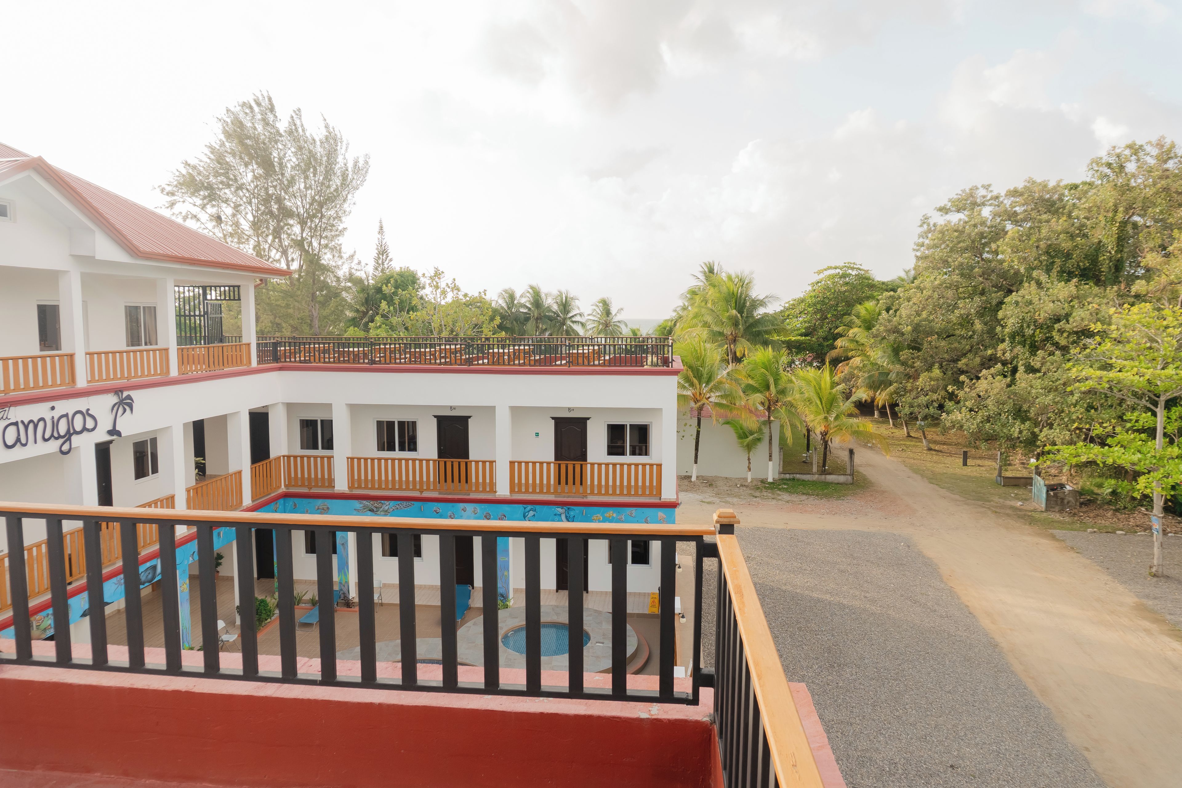 A multi-story building with balconies, a swimming pool, and a garden area with palm trees.