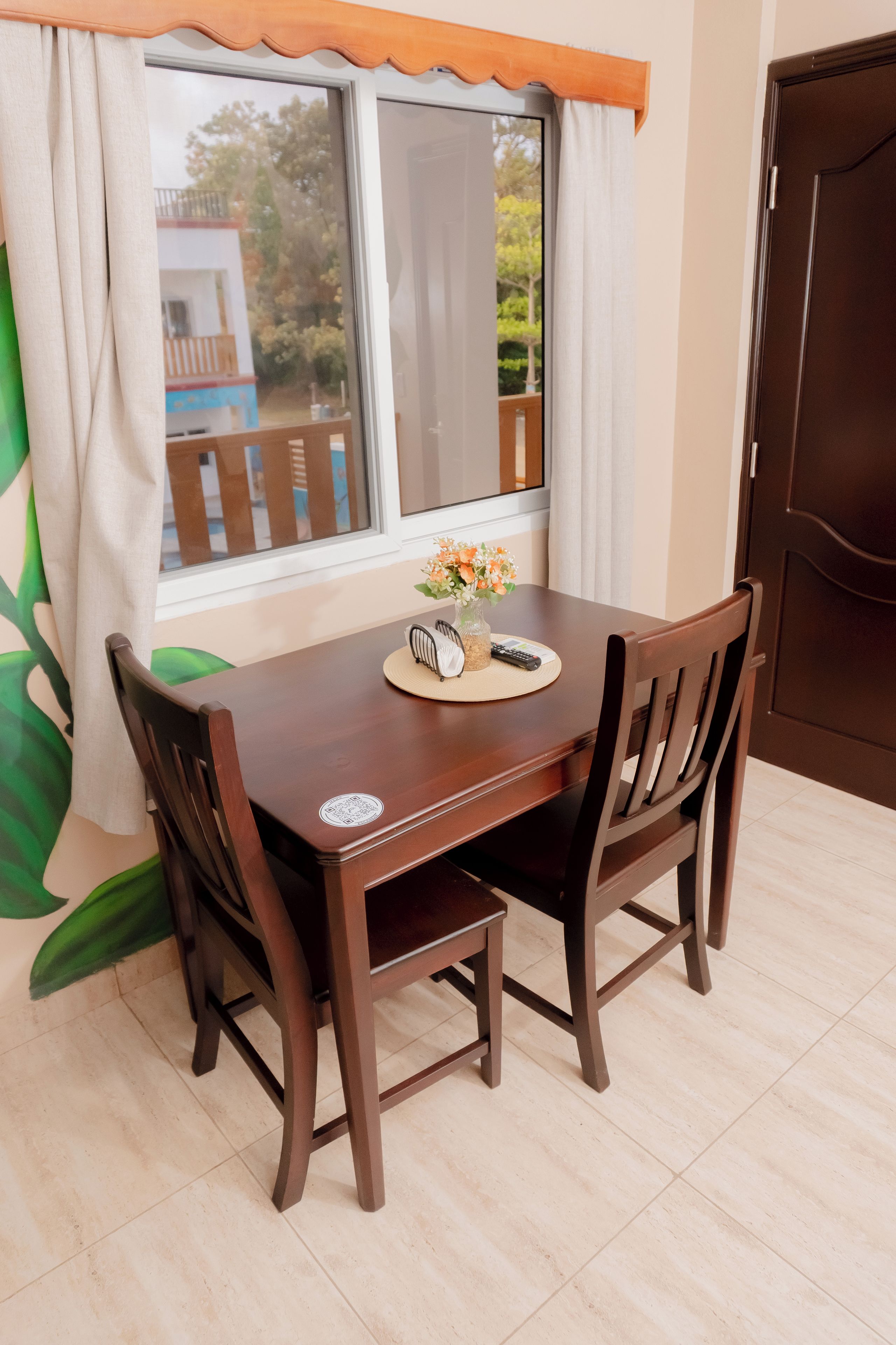 A dining table with chairs, a vase with flowers, and a remote control on the table.