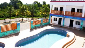 A swimming pool with a curved edge, a white building with balconies, and a fence with an underwater mural. - HOTEL LOS AMIGOS  (Puerto Cortés)