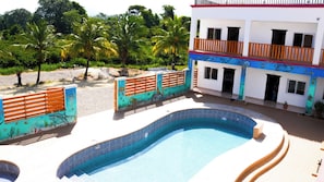 A swimming pool with a curved edge, a white building with balconies, and a fence with an underwater mural. - HOTEL LOS AMIGOS  (Puerto Cortés)
