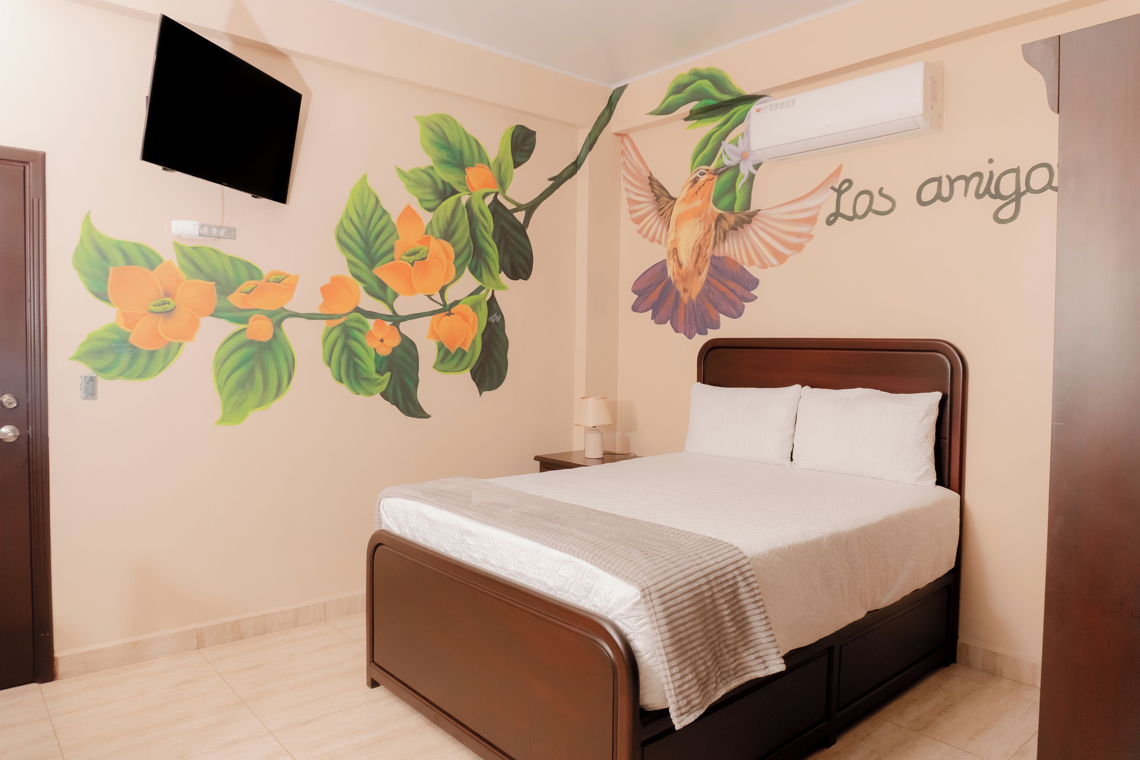 Un dormitorio con una cama, aire acondicionado de pared y un mural de flores y un pájaro.