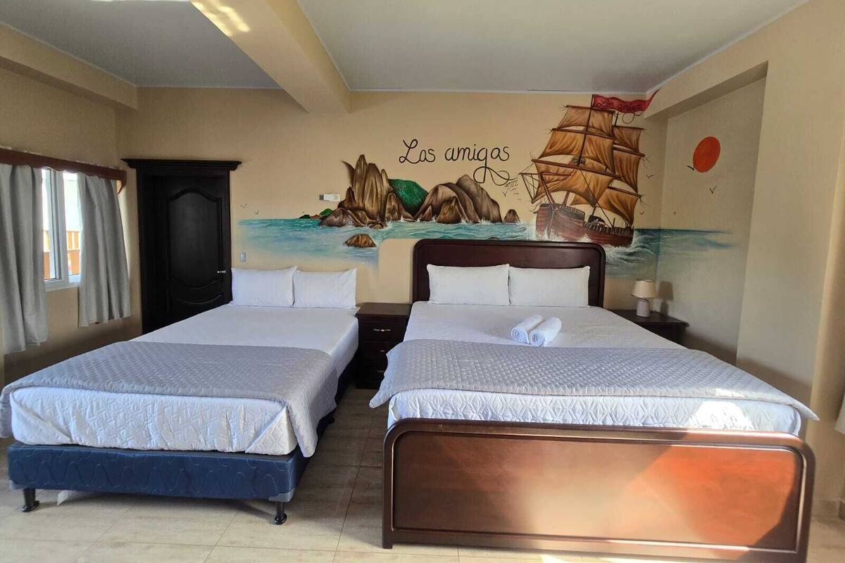 A hotel room with two beds, a mural of a ship and rocks, and a window with curtains.