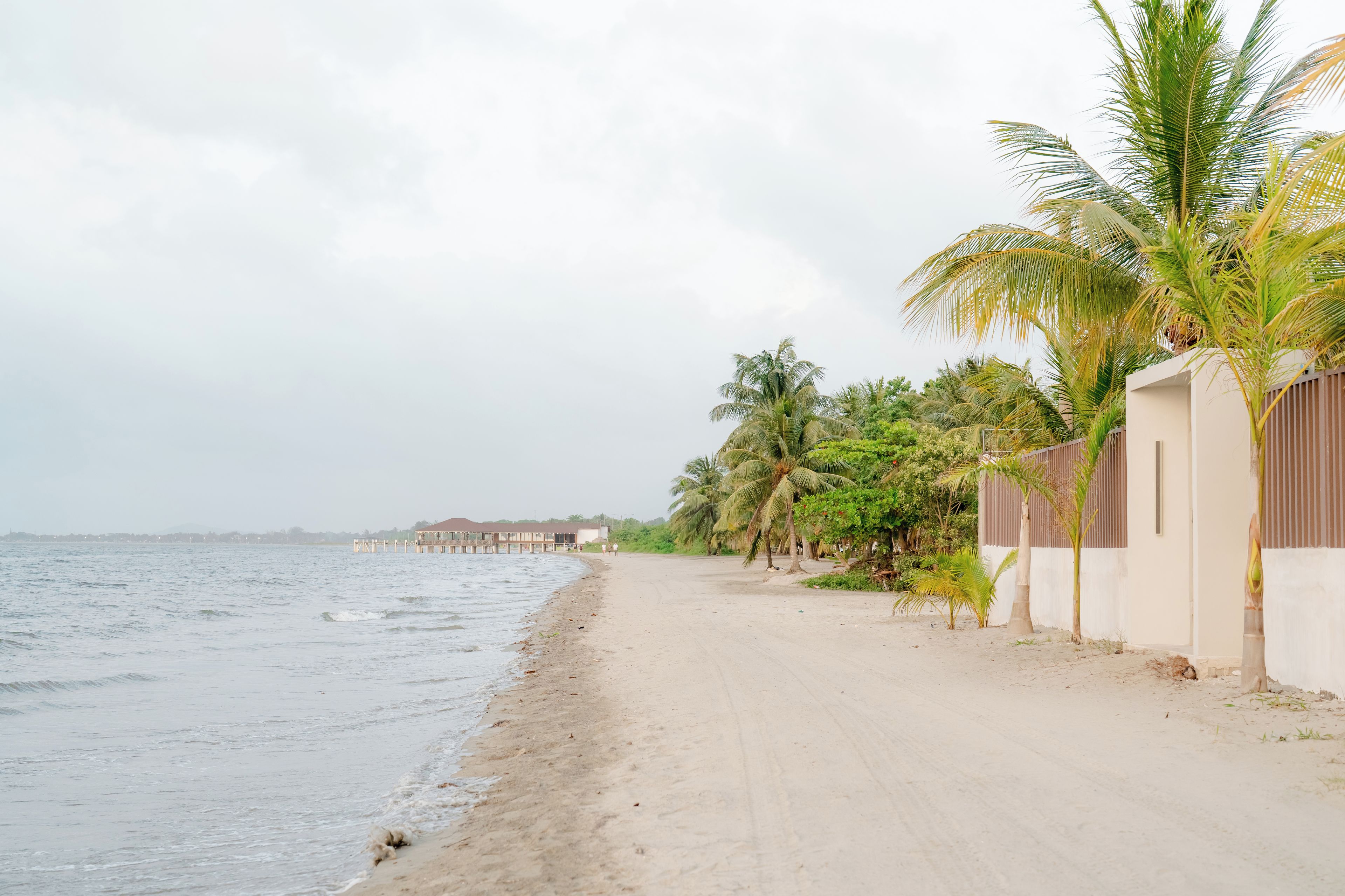 Una playa con un camino de arena, palmeras y un edificio con valla.