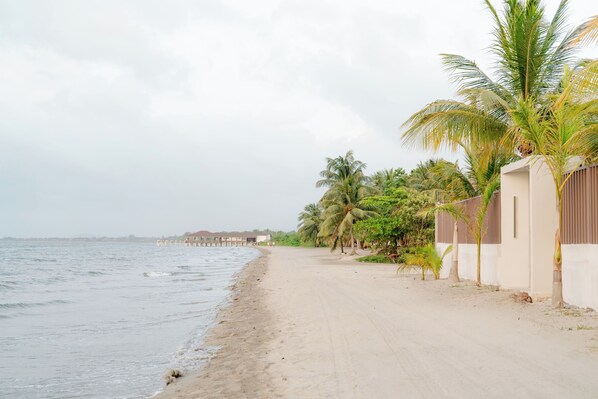 Una playa con un camino de arena, palmeras y un edificio con valla.
