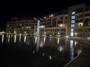Ein Nachtblick auf ein mehrstöckiges Hotel mit einem spiegelnden Pool im Vordergrund.
