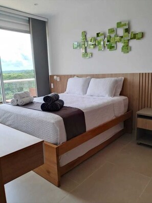 Ein Hotelzimmer mit Bett, Nachttisch, Wandbild und Blick durch ein Fenster.