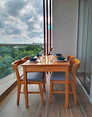 Ein Esstisch mit Stühlen auf einem Balkon mit Blick auf Grünflächen und einen bewölkten Himmel.